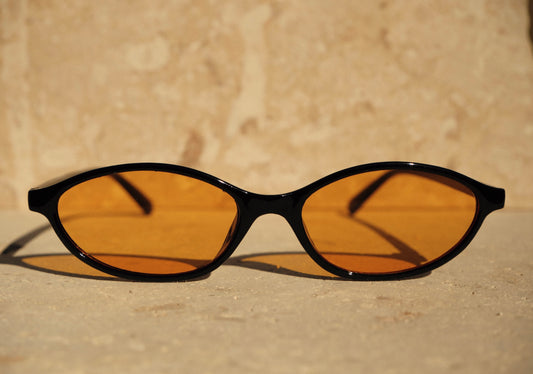 Sunglasses with black frames and orange lenses on a stone surface