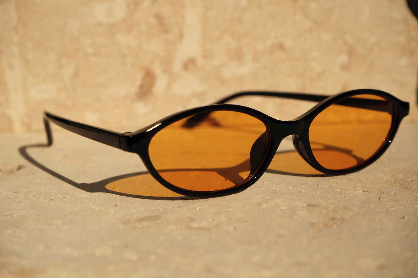 Sunglasses with black frames and amber lenses on a beige surface