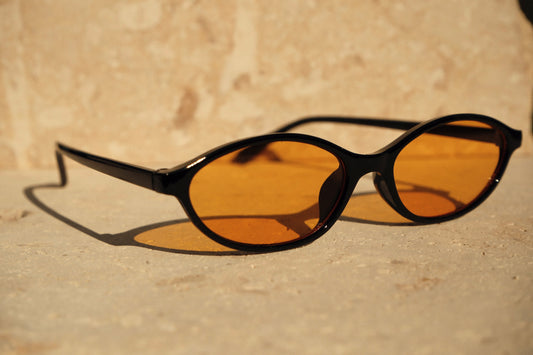 Sunglasses with black frames and amber lenses on a beige surface