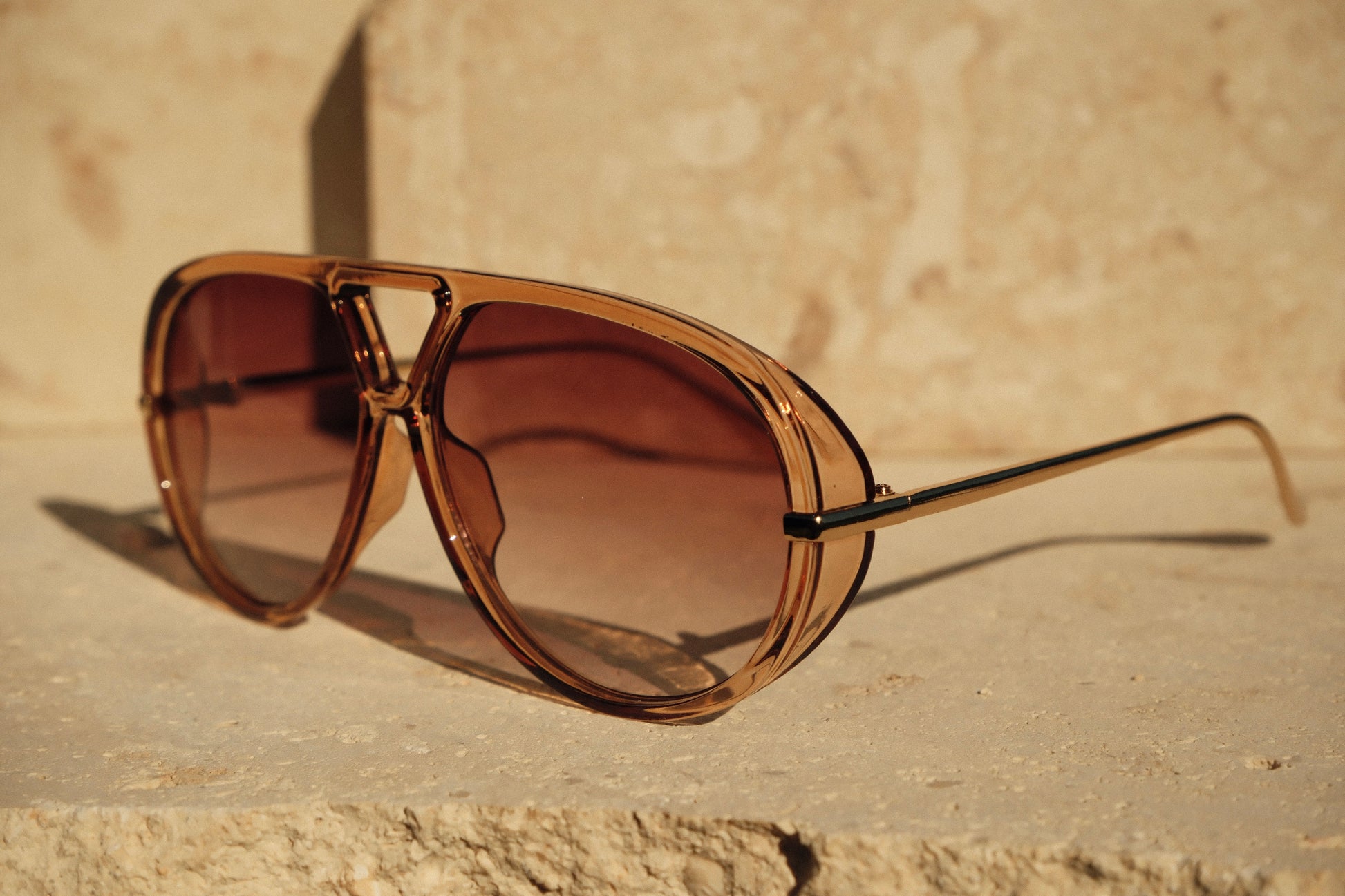 Brown sunglasses on a stone surface with a beige wall background