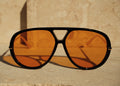 Aviator sunglasses with orange lenses and black frame on a beige background