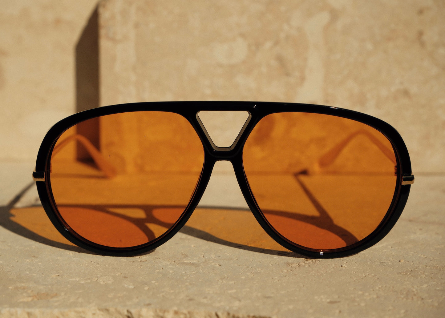 Aviator sunglasses with orange lenses and black frame on a beige background