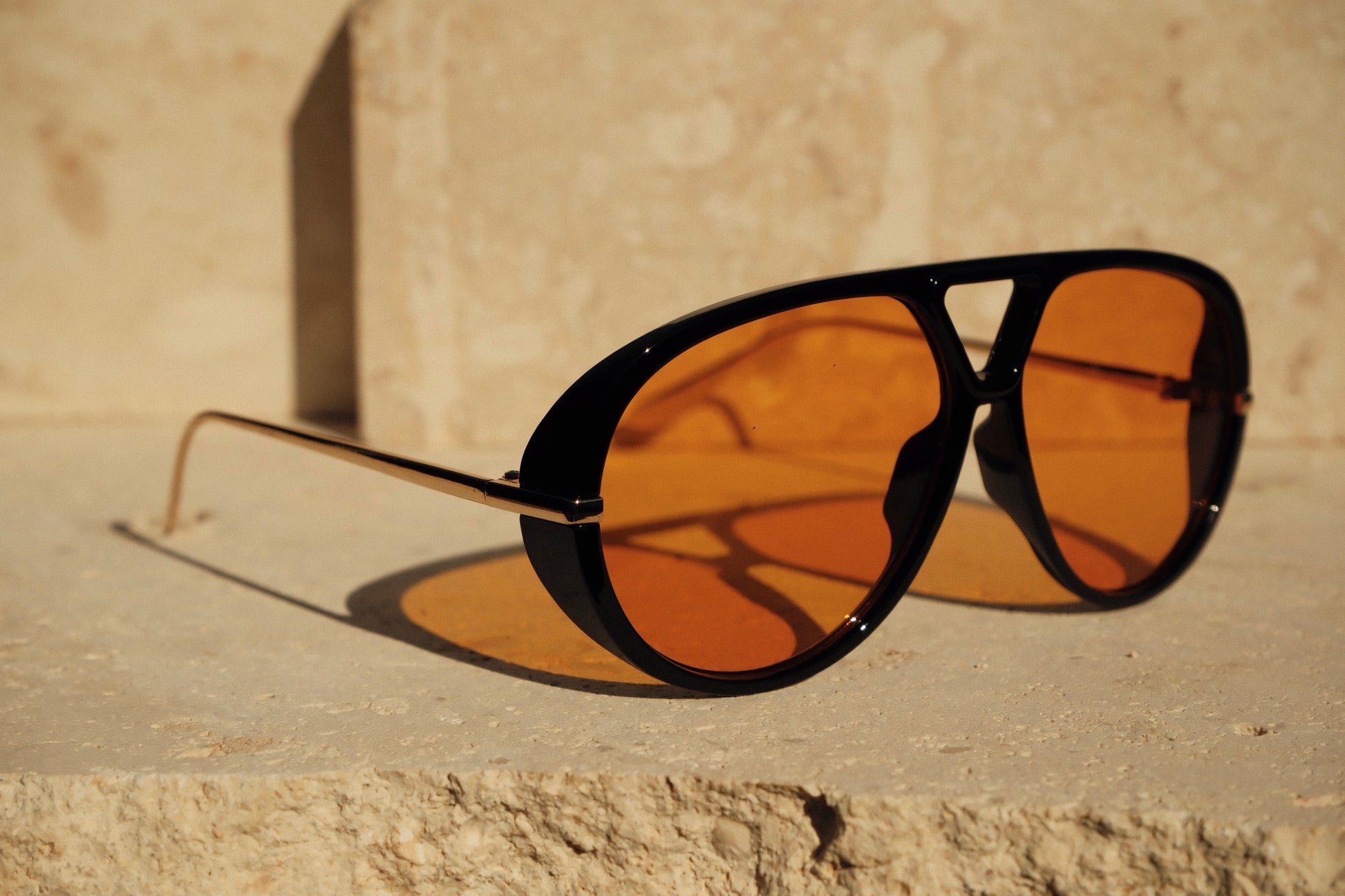Aviator sunglasses with orange lenses on a stone surface