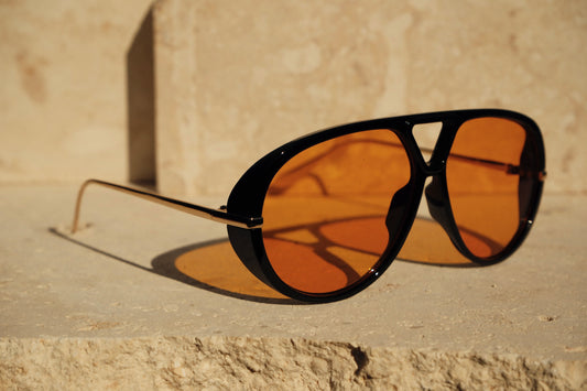 Aviator sunglasses with orange lenses on a stone surface