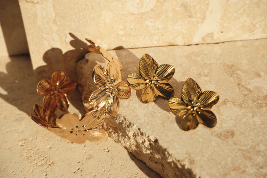 Gold floral earrings on a textured stone surface