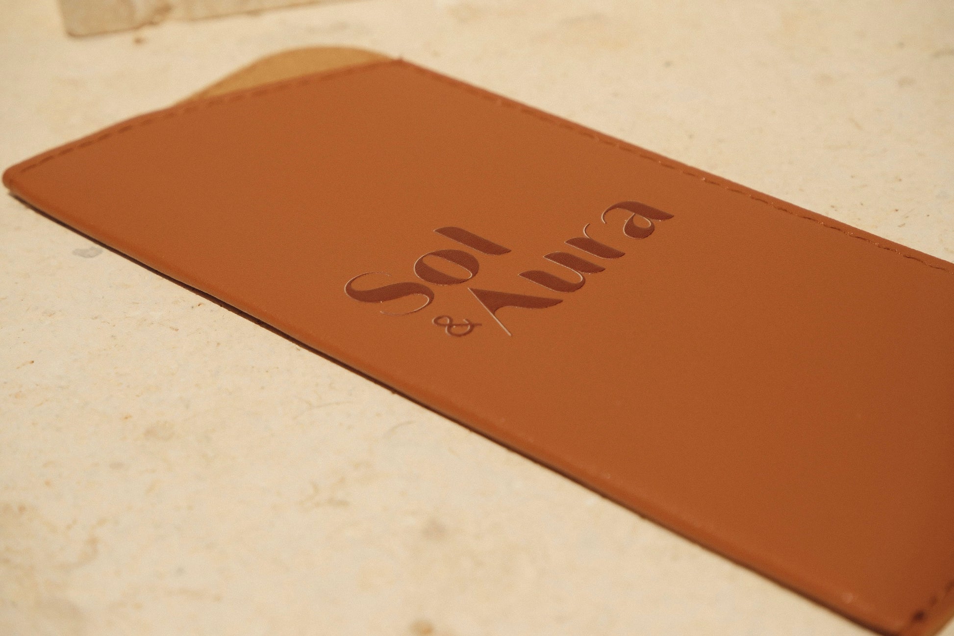 Brown leather sunglasses case with 'Sol & Aura' branding on a stone surface