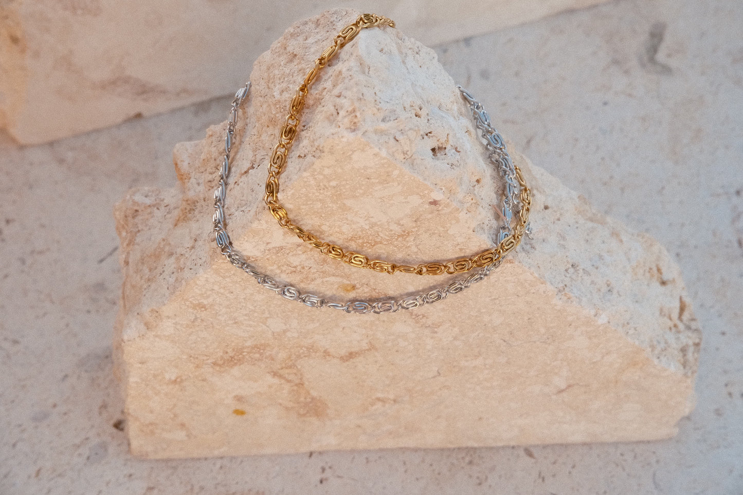 Gold and silver chain bracelets on a textured stone surface