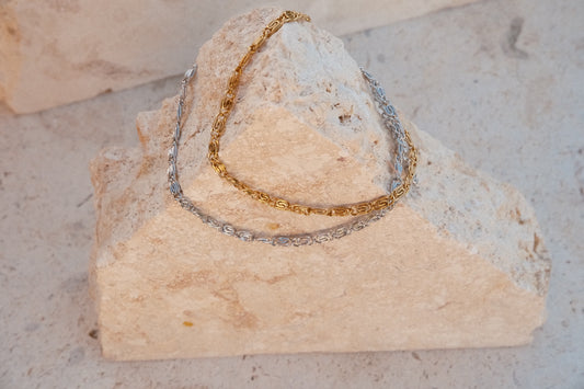 Gold and silver chain bracelets on a textured stone surface