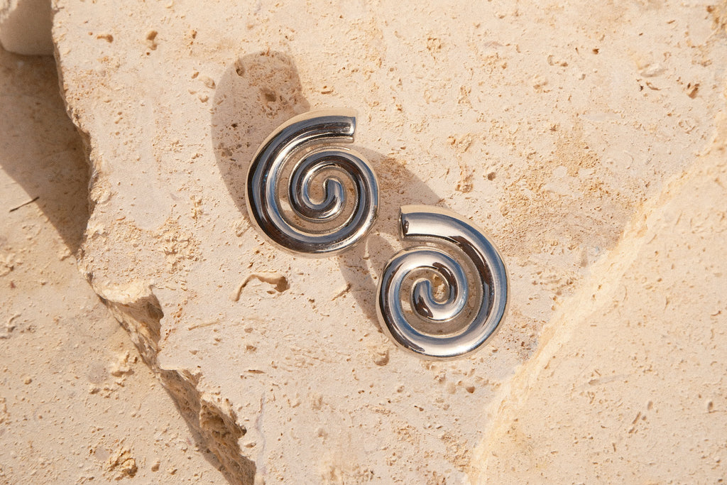 Pair of silver spiral earrings on a beige stone surface