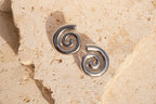 Pair of silver spiral earrings on a beige stone surface