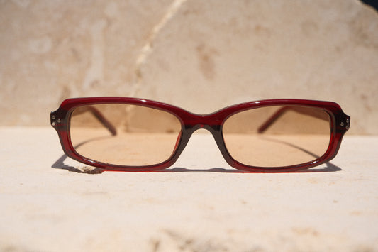 Sol & Aura - Erin Sunglasses. Red sunglasses with light tinted lens sitting on stone surface with three silver dot detailing on either side of lens