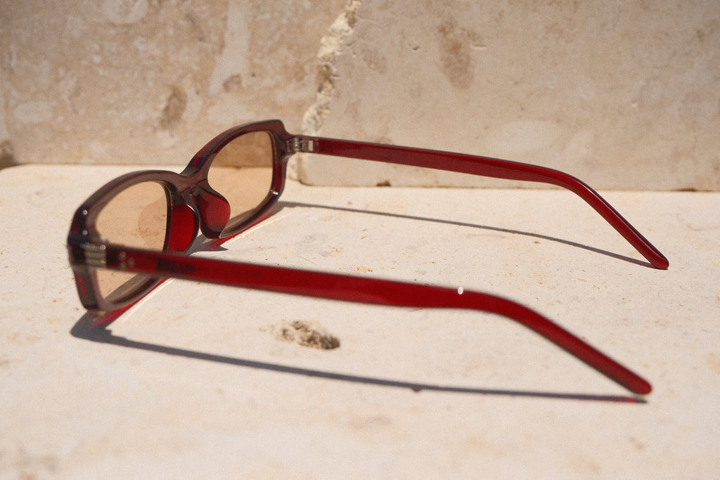 Sol & Aura - Erin Sunglasses. Red sunglasses with light tinted lens sitting on stone surface with three silver dot detailing on either side of lens