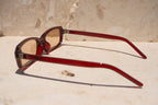 Sol & Aura - Erin Sunglasses. Red sunglasses with light tinted lens sitting on stone surface with three silver dot detailing on either side of lens