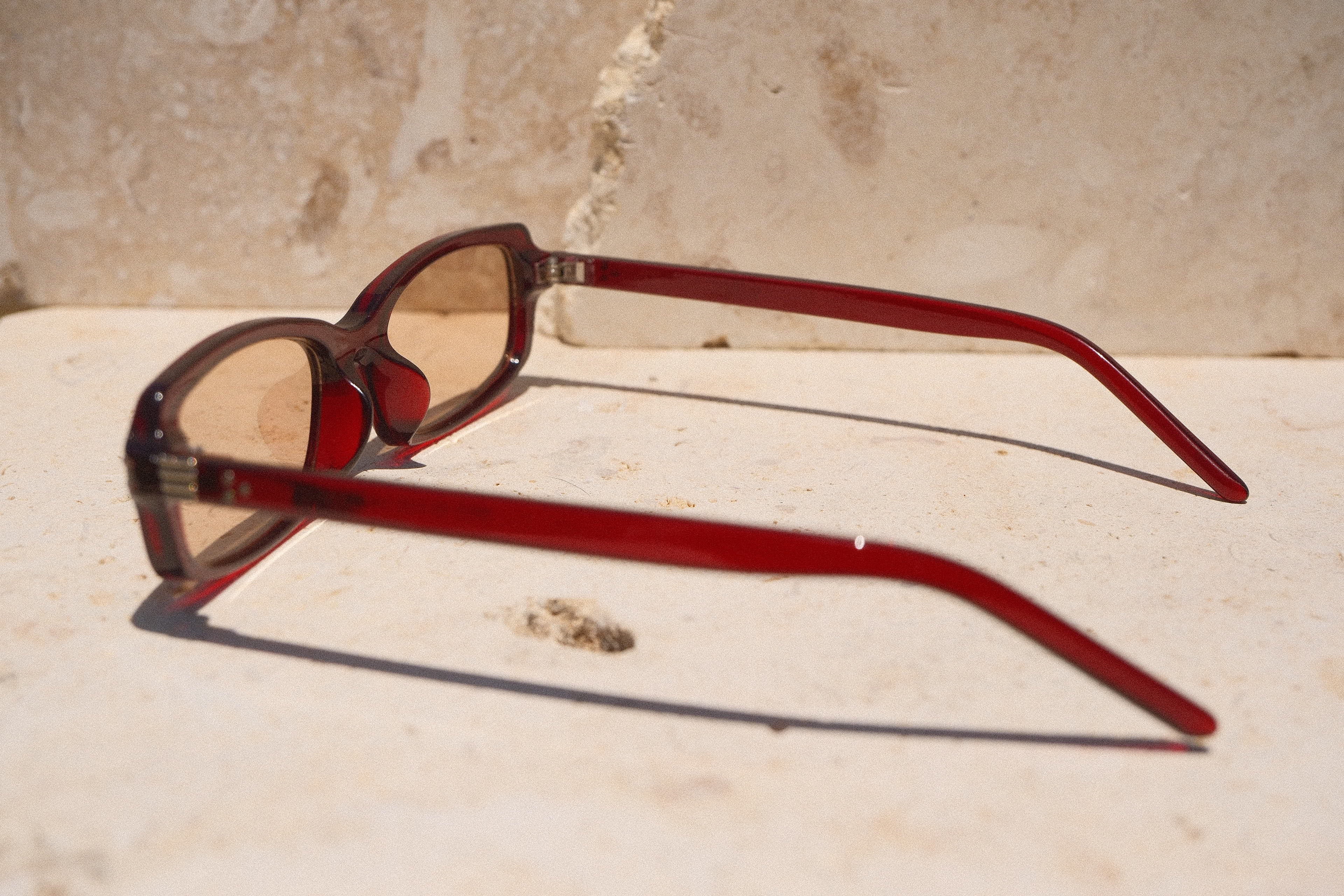 Sol & Aura - Erin Sunglasses. Red sunglasses with light tinted lens sitting on stone surface with three silver dot detailing on either side of lens