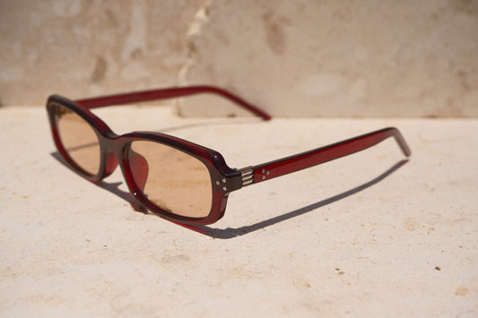 Sol & Aura - Erin Sunglasses. Red sunglasses with light tinted lens sitting on stone surface with three silver dot detailing on either side of lens