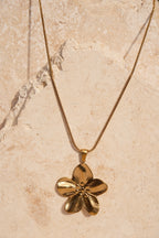 Gold flower-shaped pendant on a beige stone background