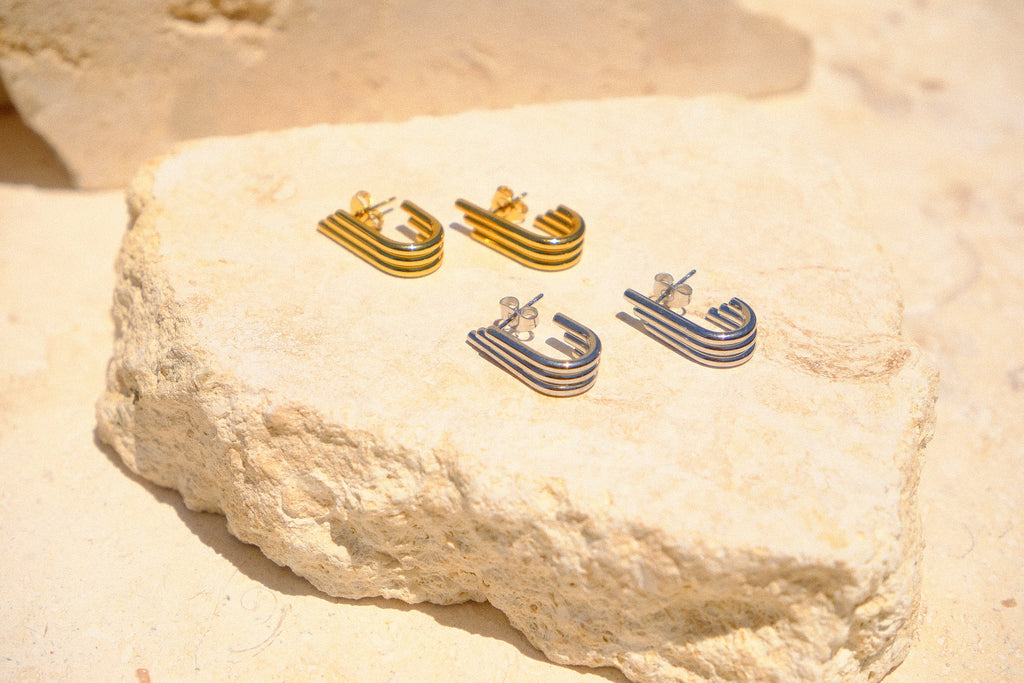 Sol & Aura - Gold & Silver 'Aria Earrings' lying on natural stone surface