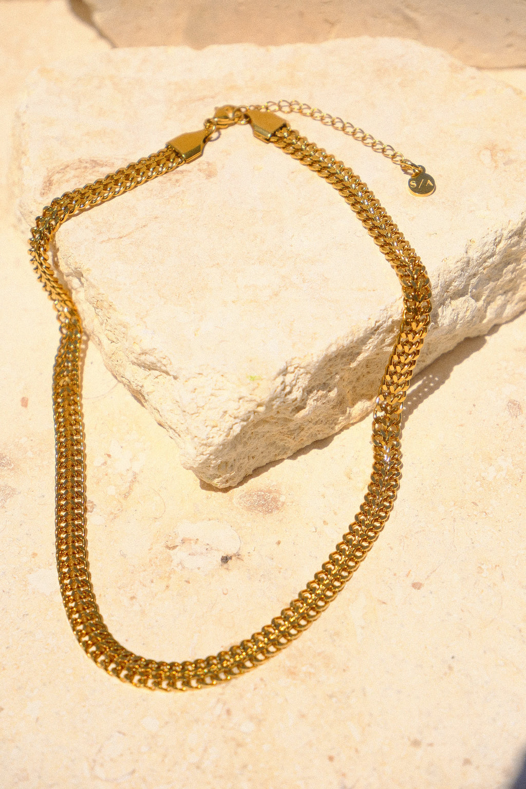 Sol & Aura - Gold chain 'Spiga Necklace' lying on stone surface with S/A logo