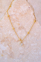 Sol & Aura - Gold anklet with a pendant hanging on a textured stone surface