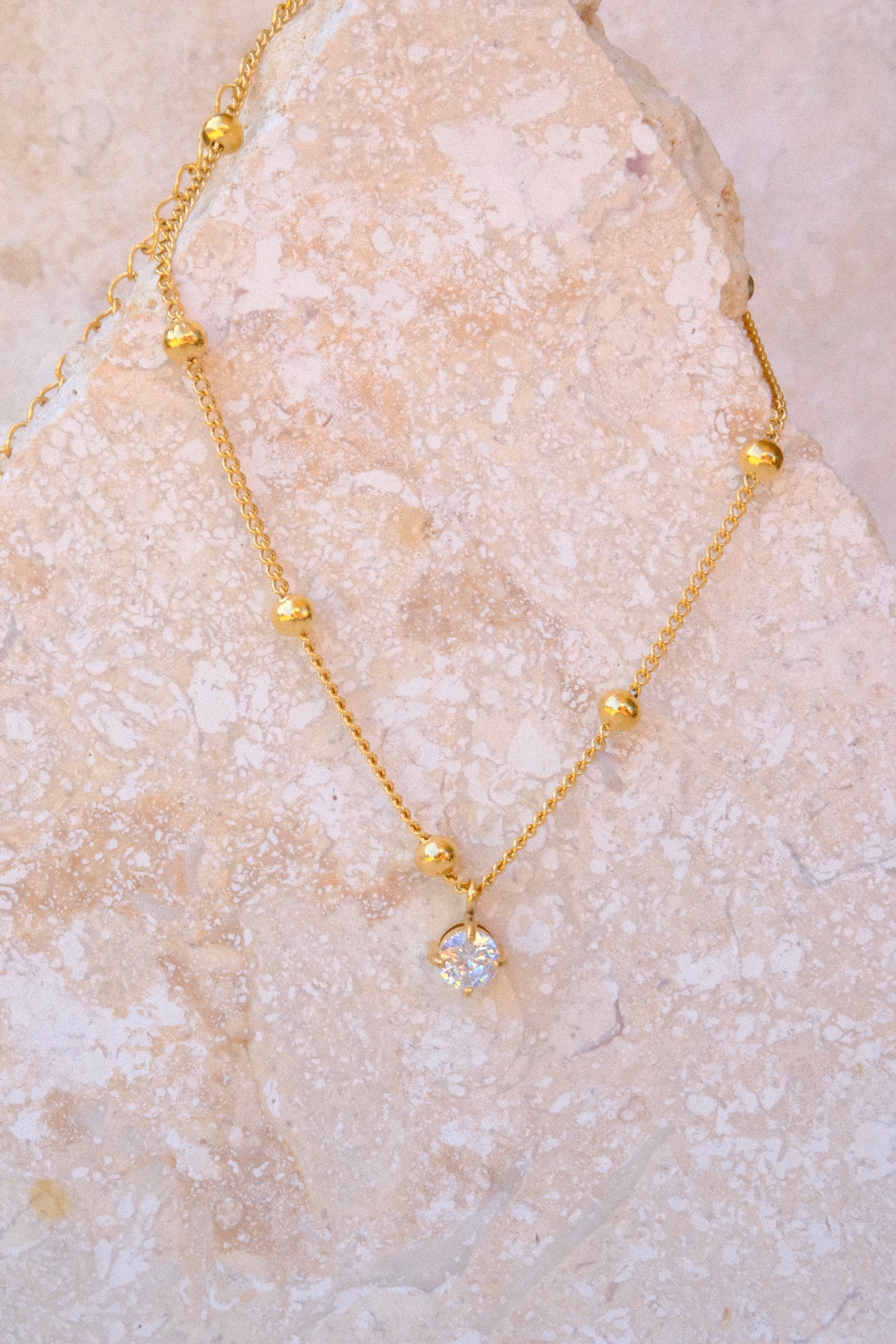 Sol & Aura - Gold anklet with a pendant hanging on a textured stone surface