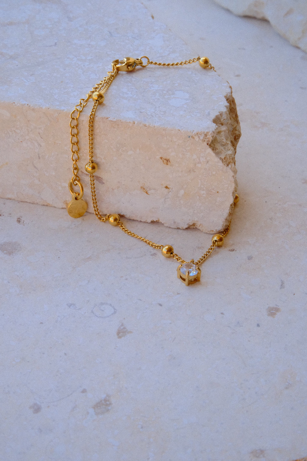 Sol & Aura - Gold anklet with a pendant hanging over a textured stone surface