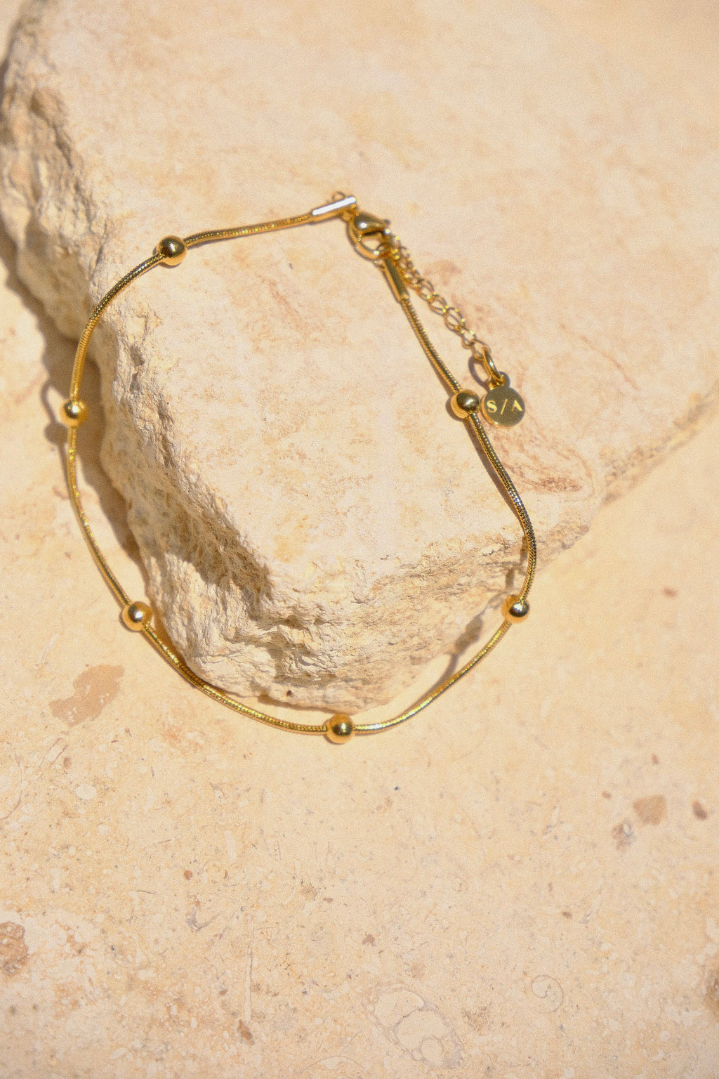 Sol & Aura - Gold anklet with gold beads lying on stone surface