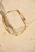Sol & Aura - Gold anklet with gold beads lying on stone surface