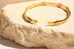 Sol & Aura - Gold bracelet with open clasp on a textured stone surface