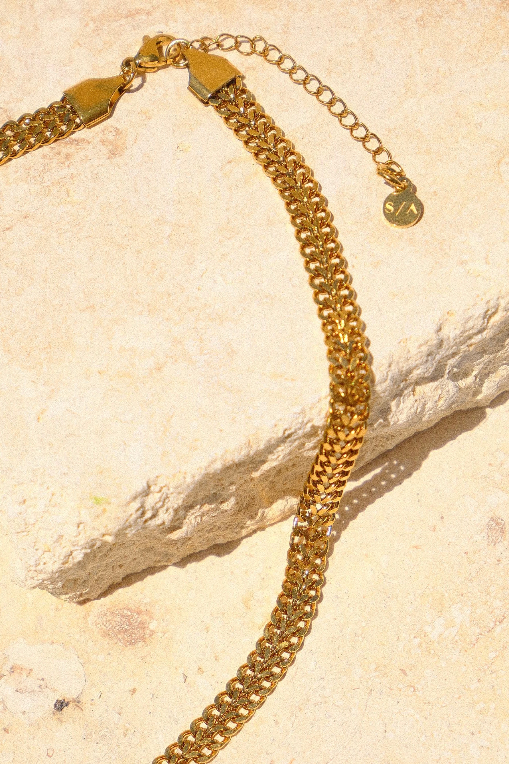Sol & Aura - Gold chain on natural stone surface with S/A logo