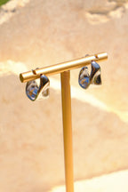 Sol & Aura - Gold earring stand with silver fluid-like earrings on a beige background