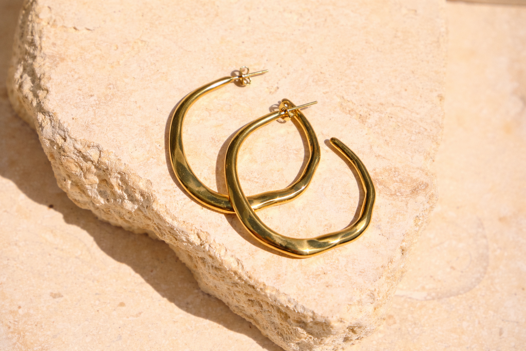Sol & Aura - Gold hoop earrings on a textured beige surface