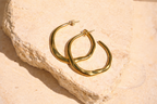 Sol & Aura - Gold hoop earrings on a textured beige surface