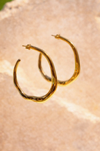 Sol & Aura - Gold hoop hanging in front of a textured stone surface