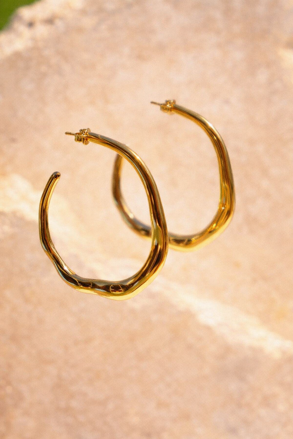 Sol & Aura - Gold hoop hanging in front of a textured stone surface