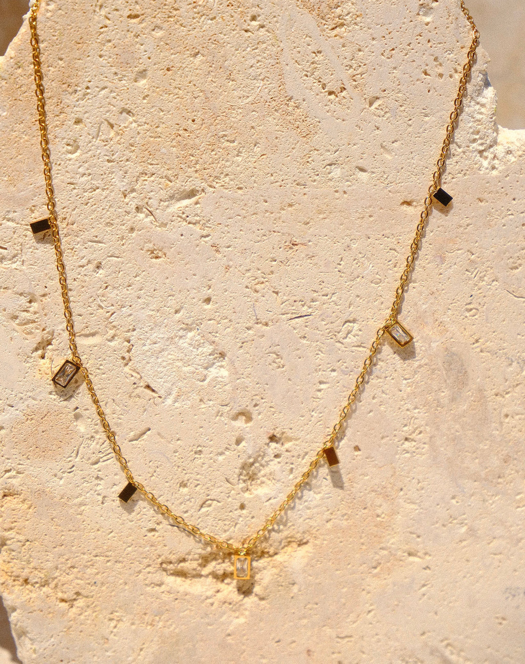 Sol & Aura - Gold necklace with square pendants on a textured stone surface