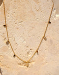 Sol & Aura - Gold necklace with square pendants on a textured stone surface