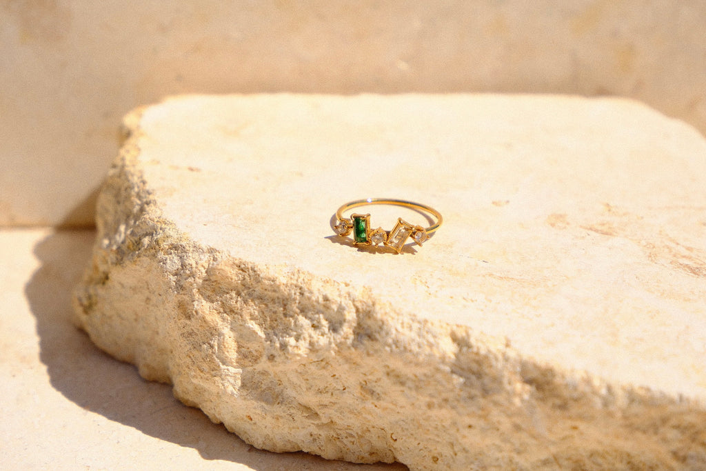 Sol & Aura - Gold ring with a green gemstone & white gemstones on a natural stone surface