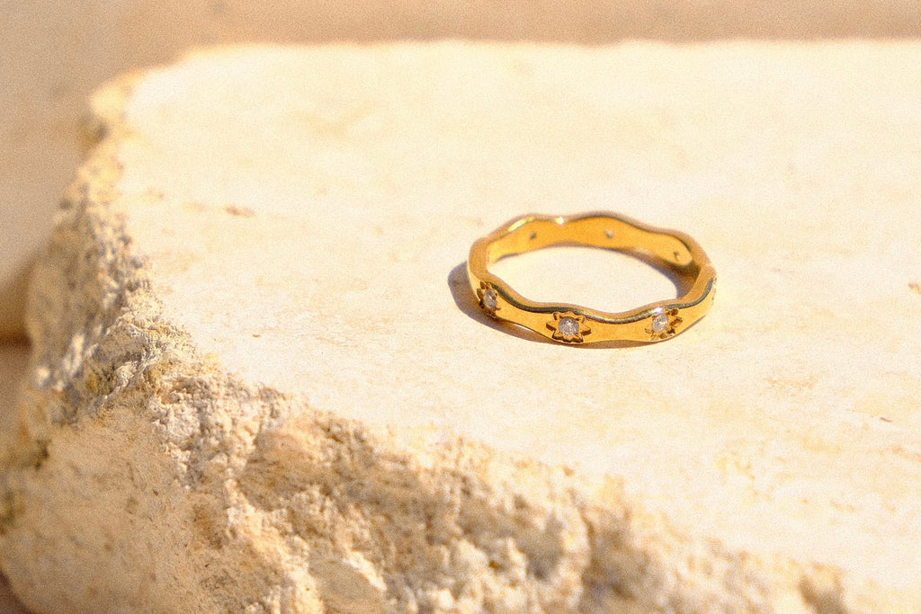 Sol & Aura - Gold ring with diamond gemstones on a textured stone surface