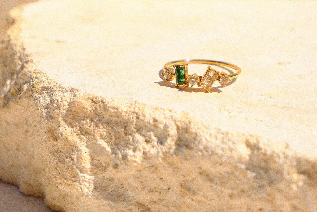 Sol & Aura - Gold ring with green gemstone on a textured beige stone surface