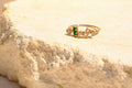 Sol & Aura - Gold ring with green gemstone on a textured beige stone surface
