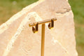 Sol & Aura - Gold stud earrings hanging on earring display against stone surface