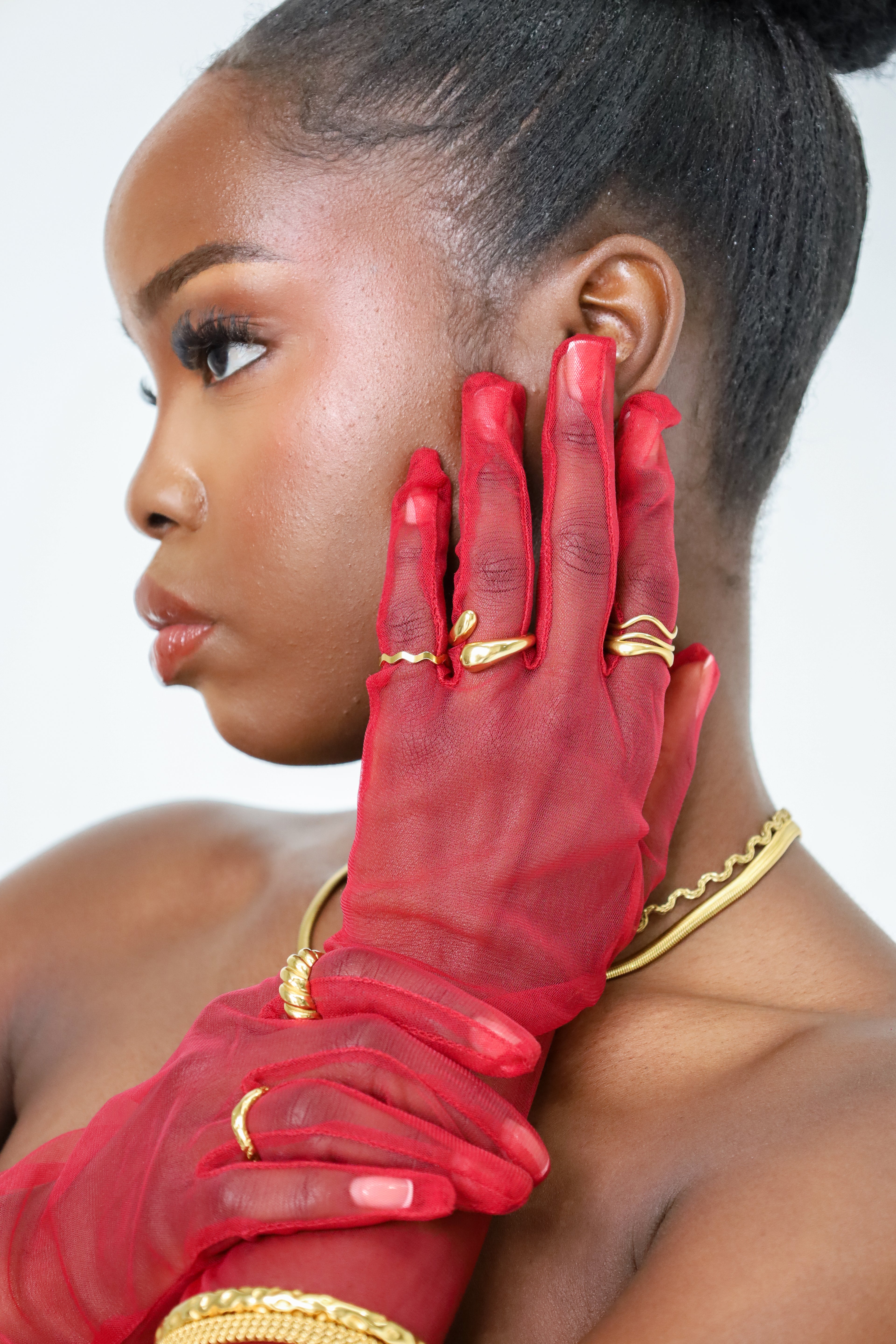 Woman wearing red gloves and gold jewelry against a white background