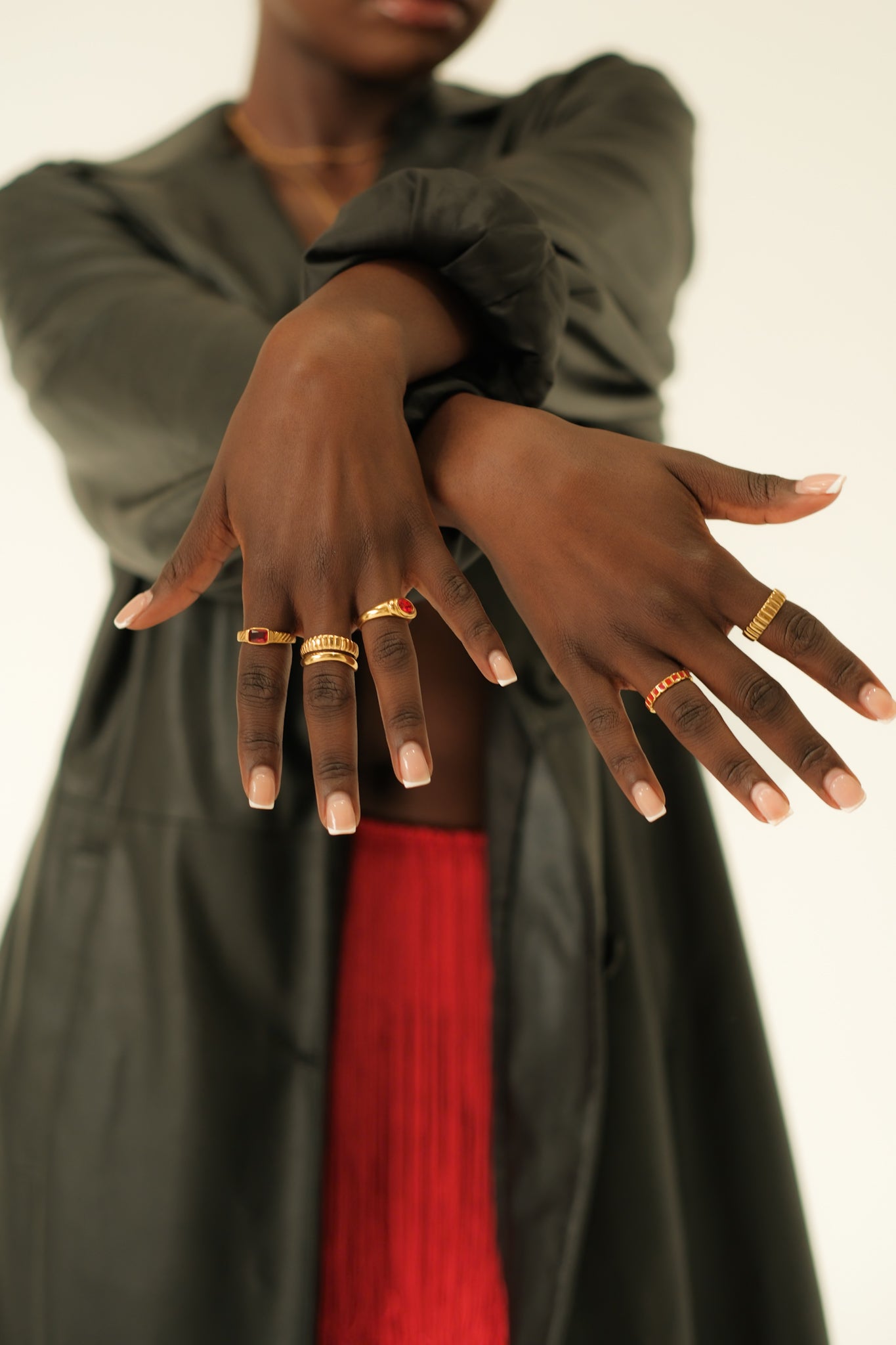 Person wearing multiple gold rings on their fingers with a neutral background