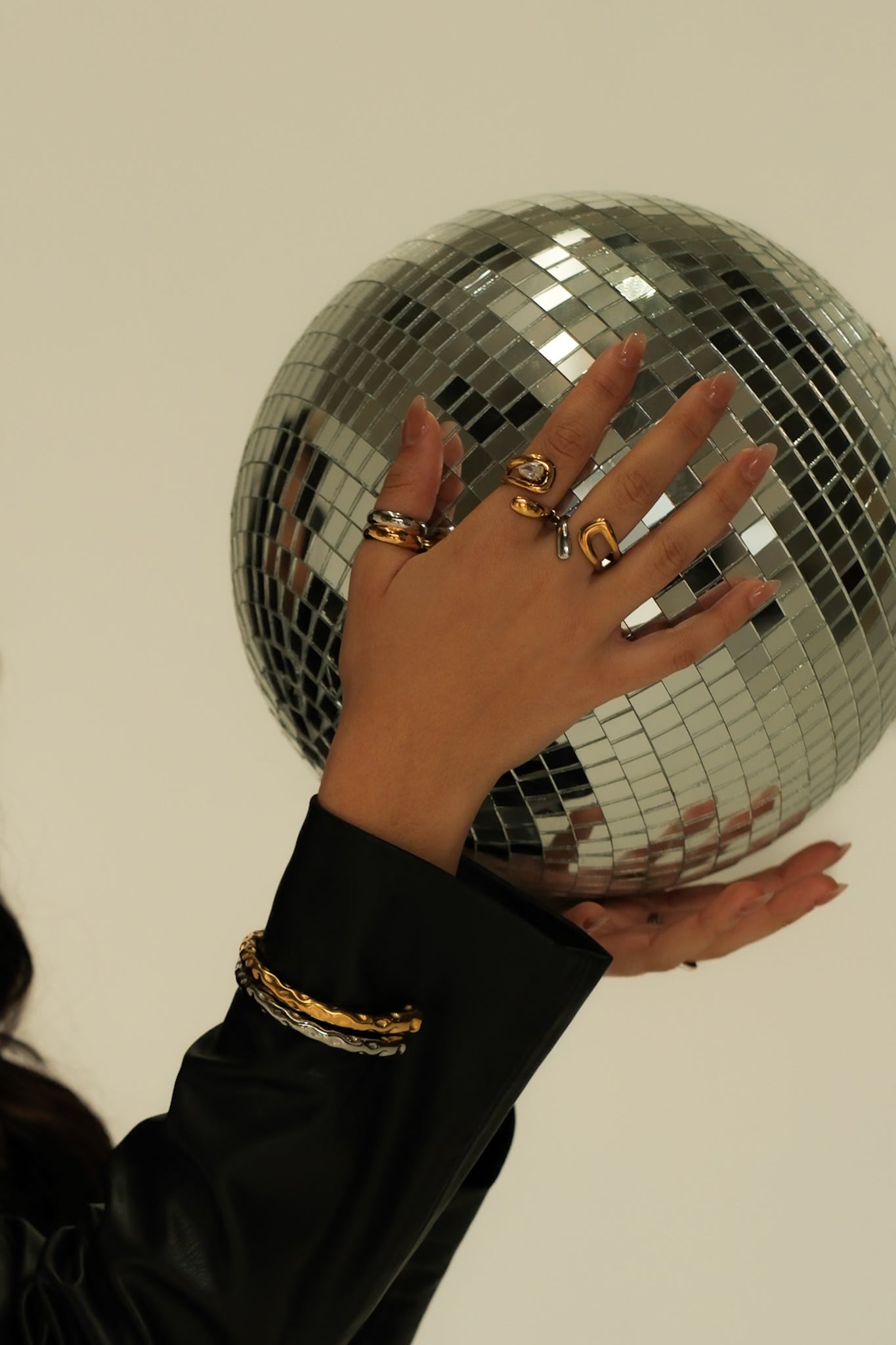 Hand wearing gold rings on a disco ball against a plain background