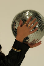 Hand with gold rings holding a disco ball against a neutral background