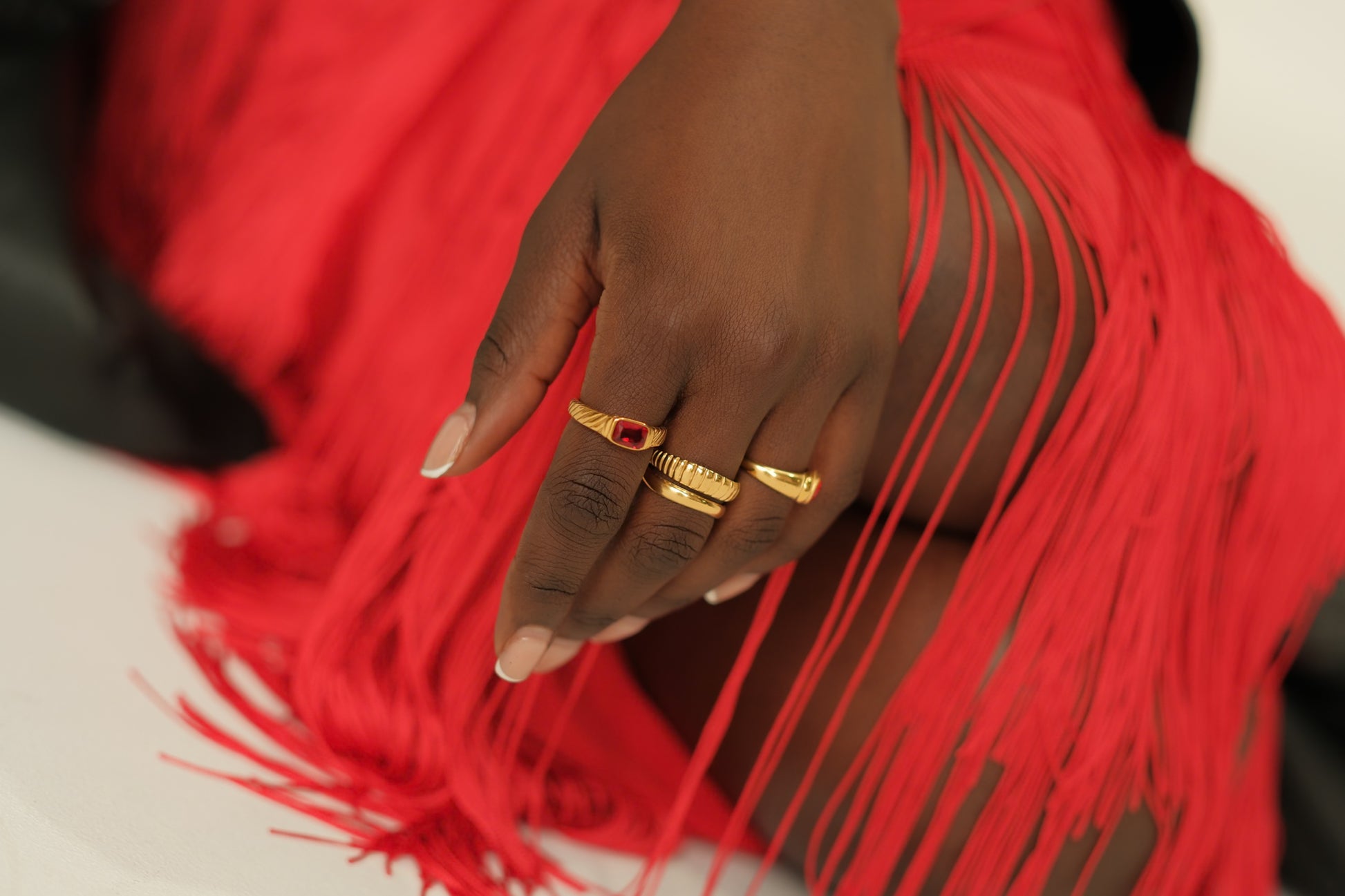 Hand with gold rings on a red fringed fabric background
