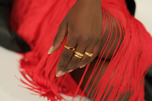Hand with gold rings on a red fringed fabric background