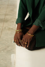 Person wearing gold bracelets and rings on a neutral background