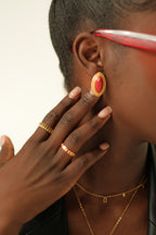 Person wearing a gold earring with a red gemstone, gold ring, and necklace.