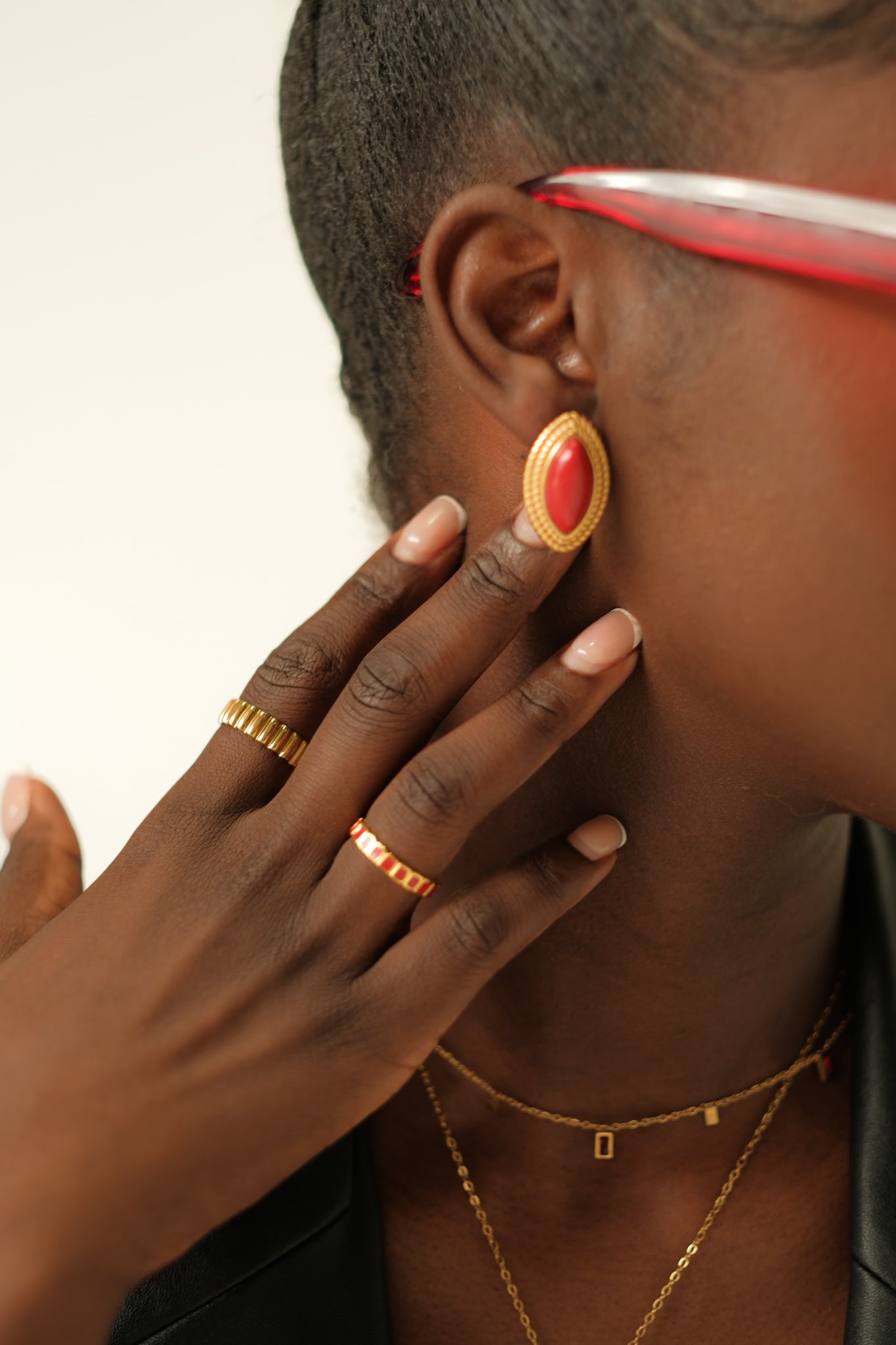 Person wearing a gold earring with a red gemstone, gold ring, and necklace.